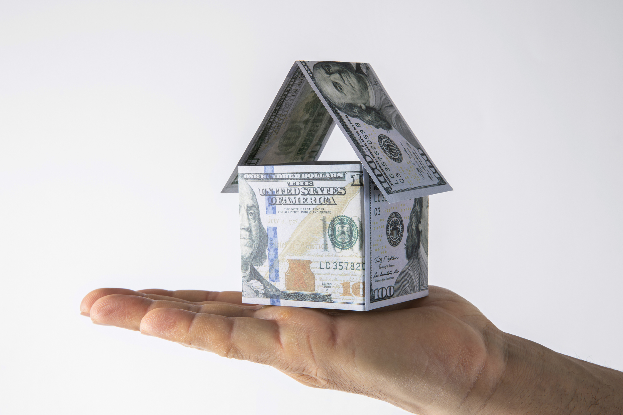 An open hand holding a small house-shaped structure made of hundred-dollar bills, symbolizing home equity and financial concepts discussed in the Southern Oregon real estate market blog.